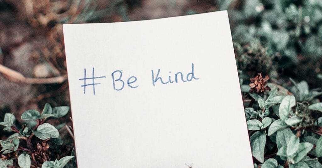 Close-up of an inspirational note with 'Be Kind' hashtag placed on lush green grass.