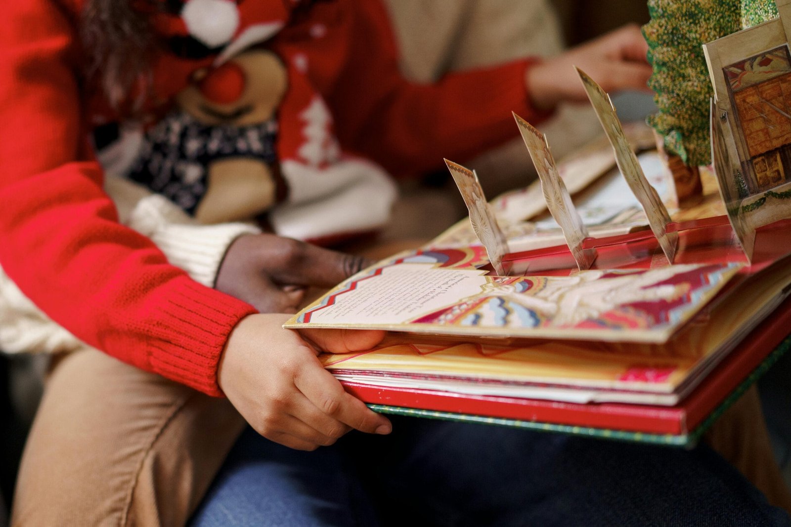 A father and child share a cozy moment reading a festive Christmas pop-up book indoors.
